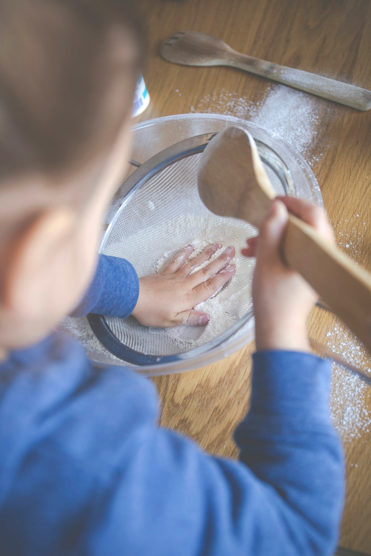 child in blue long sleeve shirt holding brown wooden rolling pin