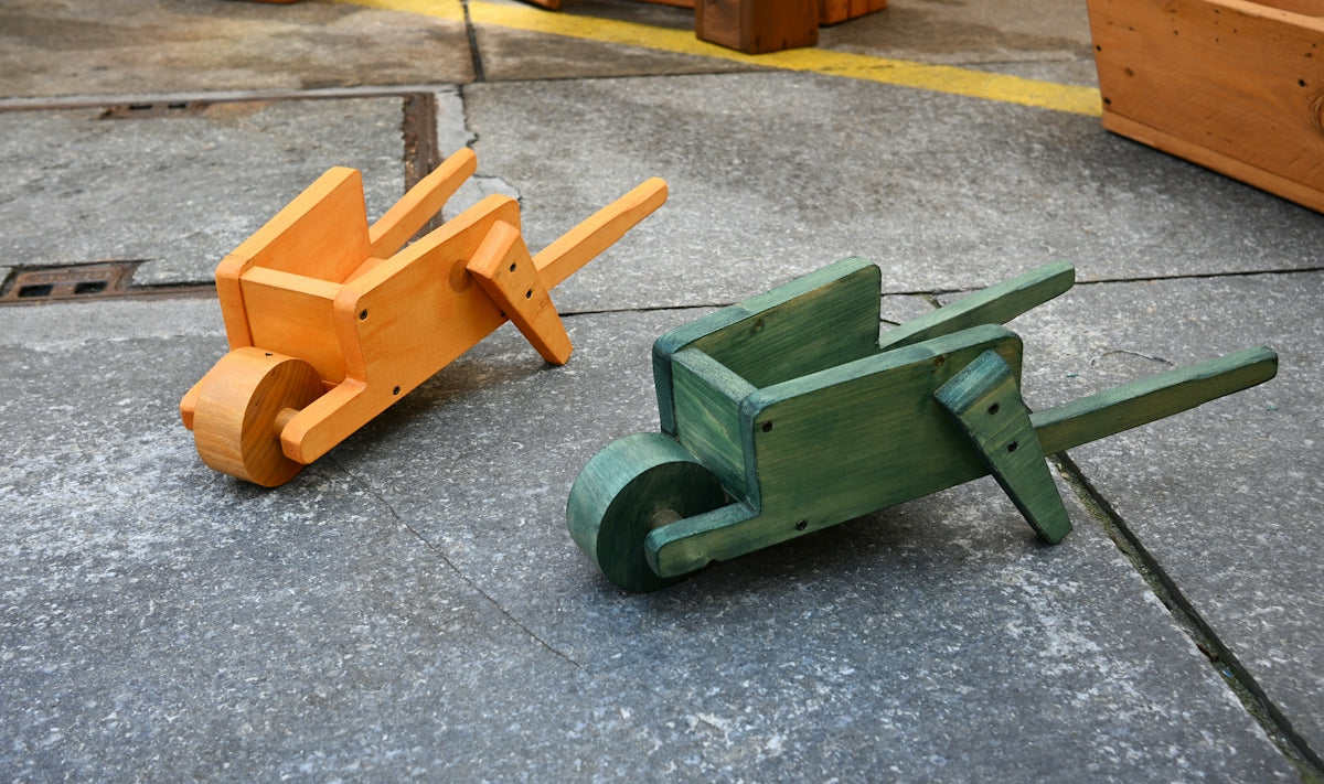 Two colorful wooden toy wheelbarrows on a concrete surface