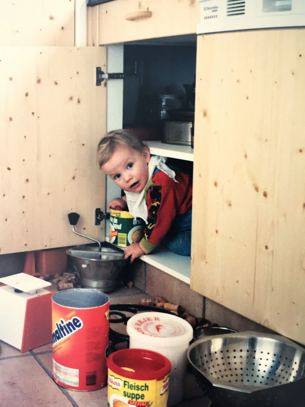 A curious child peeking from inside a kitchen cabinet.